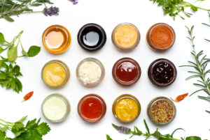 Large collection of sauces and spiced spreads in small jars isolated flat lay. Various herbs and dressings as mayo ketchup mustard soy sauce and many more
