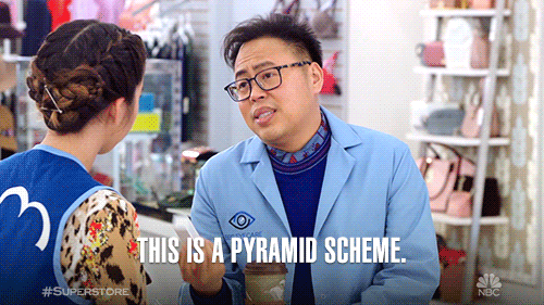 Store employee wearing a blue vest telling another worker that she’s selling a pyramid scheme