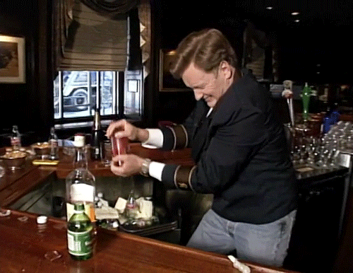 Man wearing a uniform jacket shaking a cocktail behind a bar