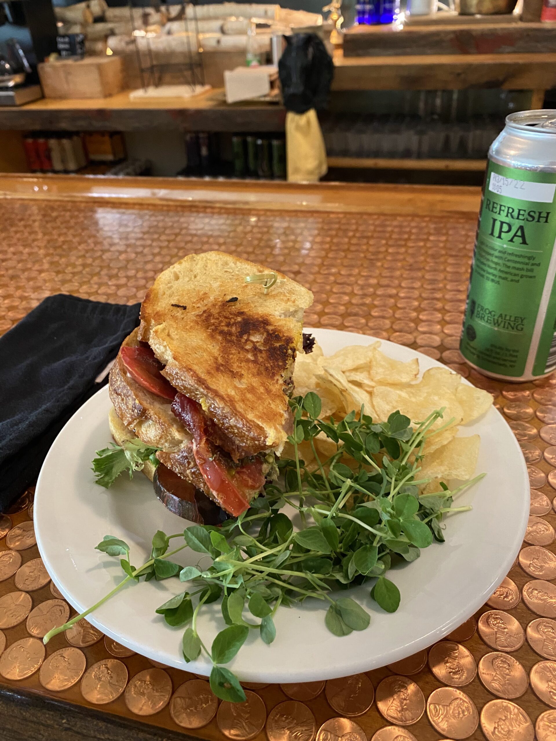 A sandwich with a side of salad, potato chips, and a can of beer