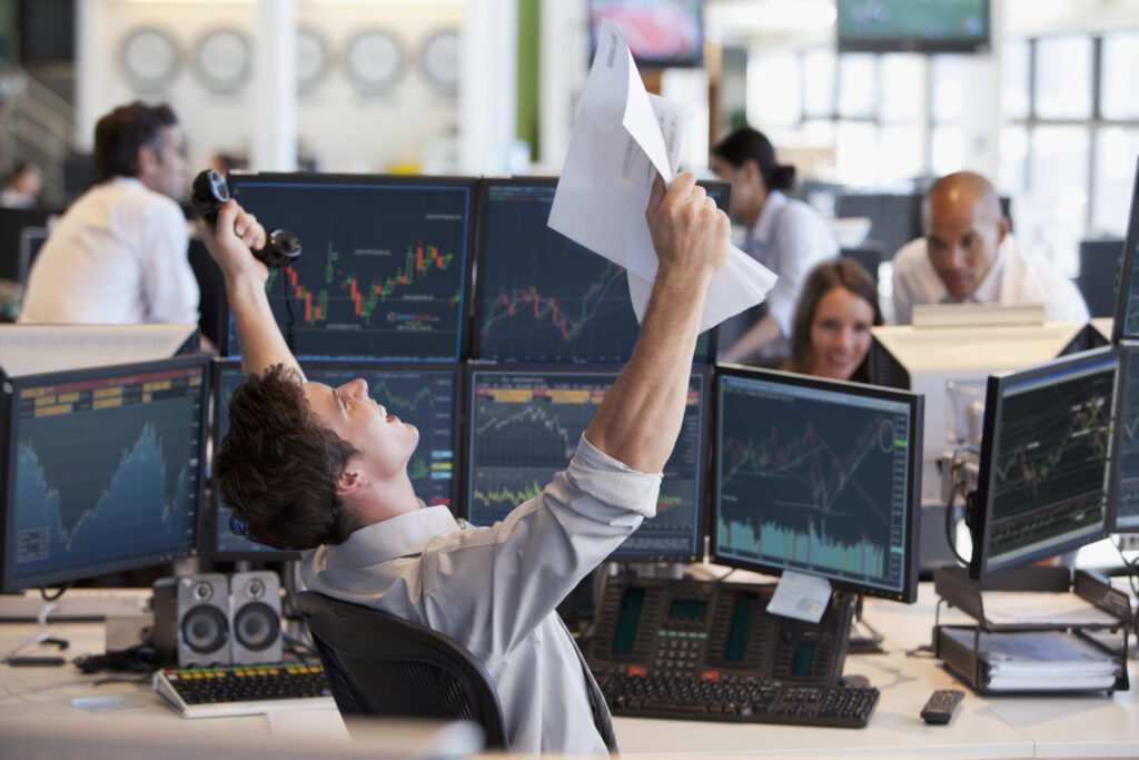 Broker in a suit celebrating in front of multiple monitors