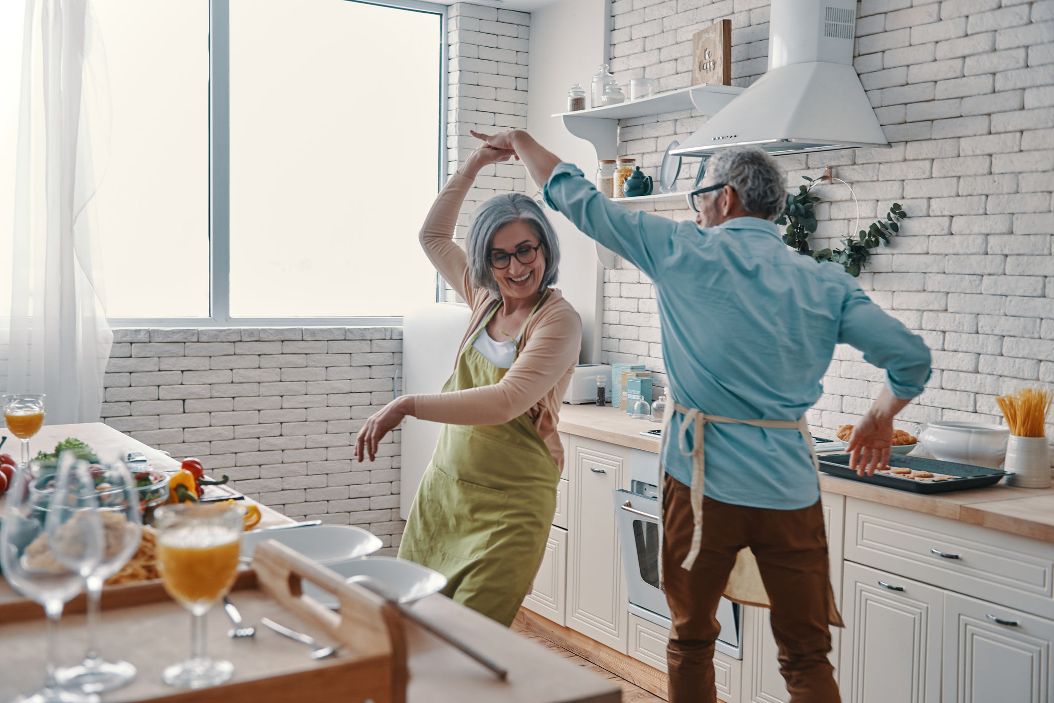 Retirement-age couple wearing aprons dancing in a kitchen