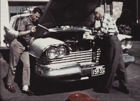 Vintage archival footage of two men repairing the engine of a a classic car